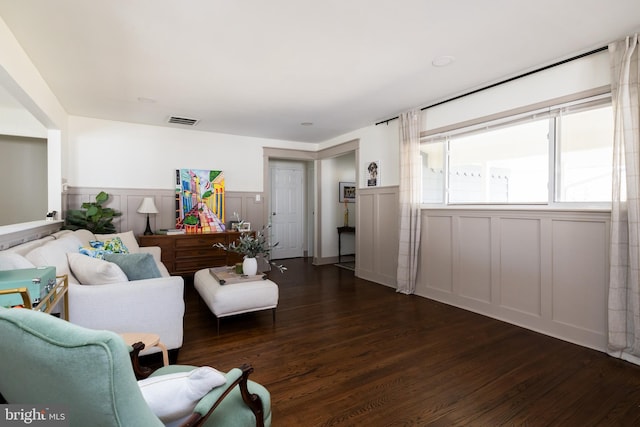 living area featuring dark wood-type flooring, wainscoting, visible vents, and a decorative wall