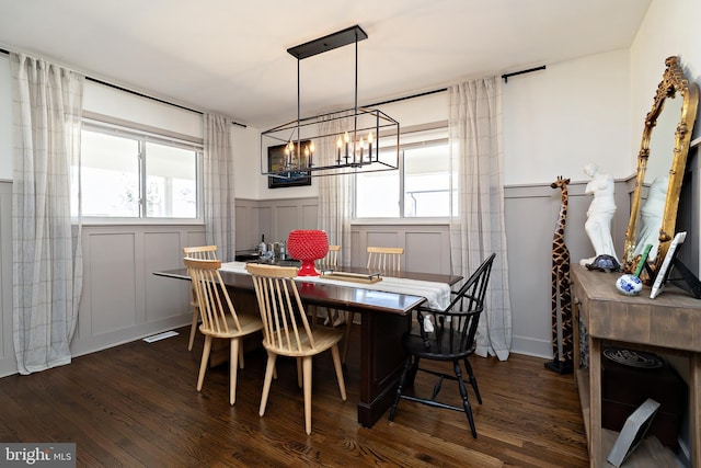 dining space featuring a wainscoted wall, dark wood finished floors, and a decorative wall