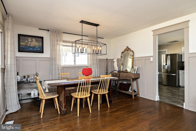 dining area with visible vents, a decorative wall, dark wood-type flooring, and wainscoting