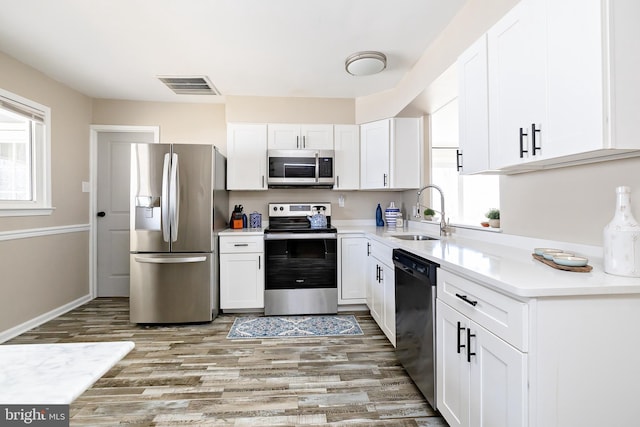 kitchen with stainless steel appliances, a sink, visible vents, white cabinets, and light wood-type flooring