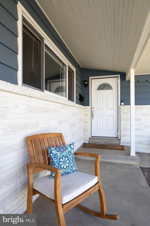 doorway to property featuring covered porch and brick siding