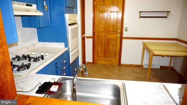 kitchen featuring white appliances, light countertops, under cabinet range hood, a warming drawer, and blue cabinets