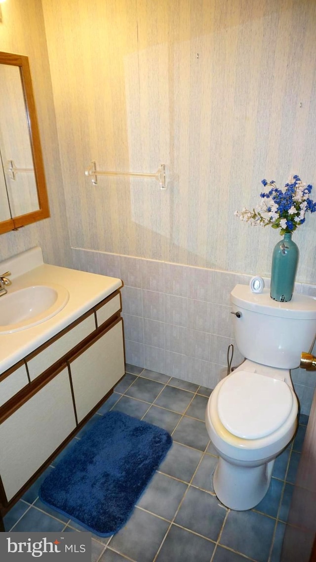 half bath with wallpapered walls, toilet, vanity, and tile patterned flooring