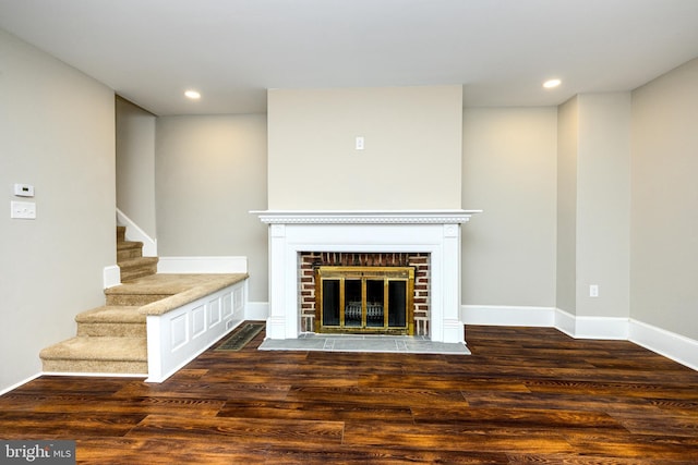 unfurnished living room with a brick fireplace, stairway, wood finished floors, and recessed lighting