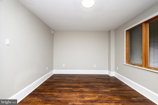 spare room with dark wood-style flooring, visible vents, and baseboards