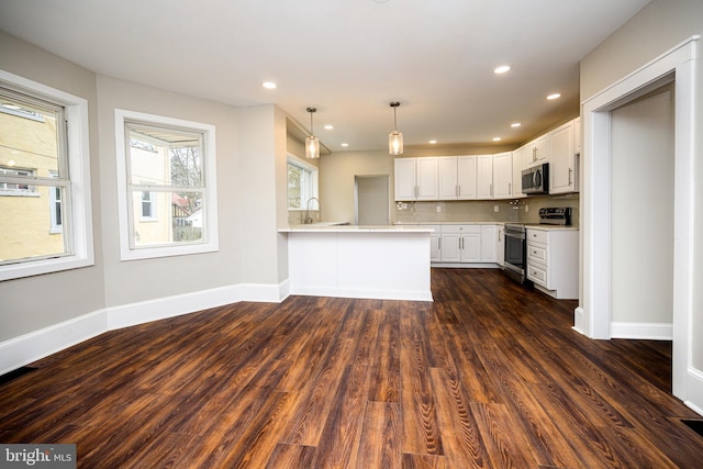 kitchen with a peninsula, dark wood-style flooring, stainless steel appliances, and light countertops