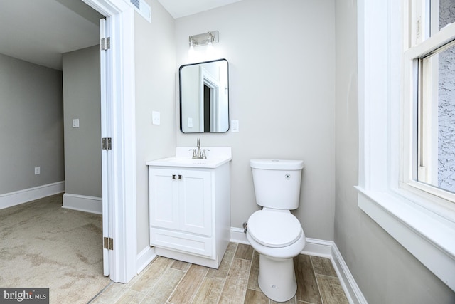 half bathroom with visible vents, toilet, wood tiled floor, vanity, and baseboards