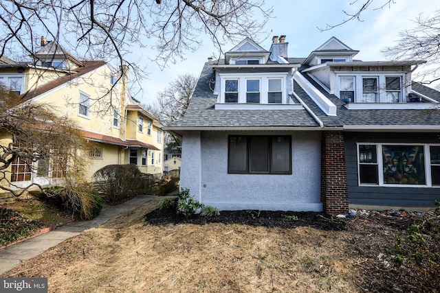 exterior space with roof with shingles, a chimney, and stucco siding