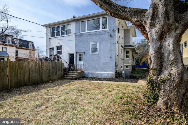 rear view of house with fence, central AC, and stucco siding