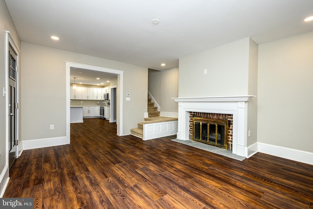 unfurnished living room with recessed lighting, dark wood-type flooring, baseboards, stairs, and a brick fireplace