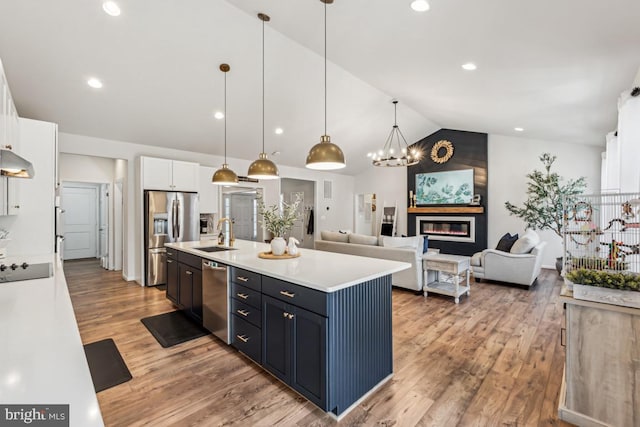 kitchen with stainless steel appliances, light countertops, a large fireplace, white cabinets, and a sink