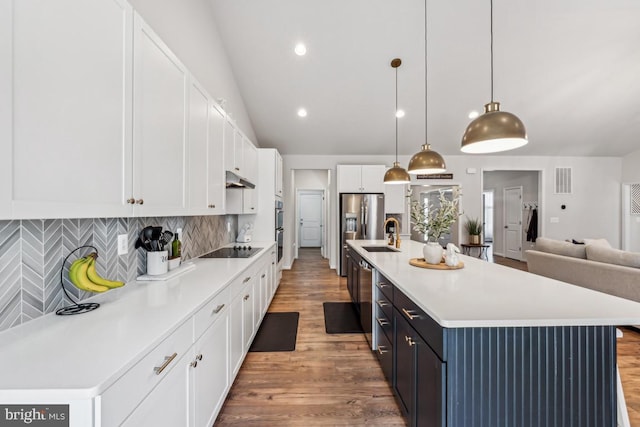 kitchen with light countertops, appliances with stainless steel finishes, open floor plan, white cabinets, and under cabinet range hood