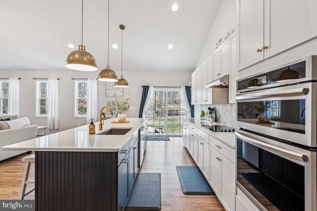 kitchen with stainless steel appliances, light countertops, white cabinets, a sink, and under cabinet range hood