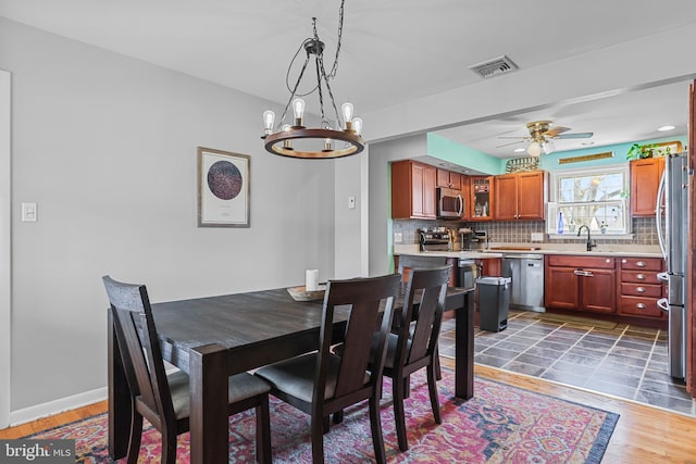 dining space with visible vents, baseboards, wood finished floors, and ceiling fan with notable chandelier