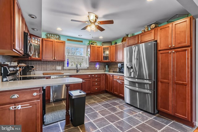 kitchen featuring backsplash, glass insert cabinets, light countertops, brown cabinetry, and stainless steel appliances