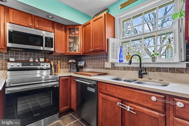 kitchen featuring a sink, decorative backsplash, light countertops, glass insert cabinets, and appliances with stainless steel finishes