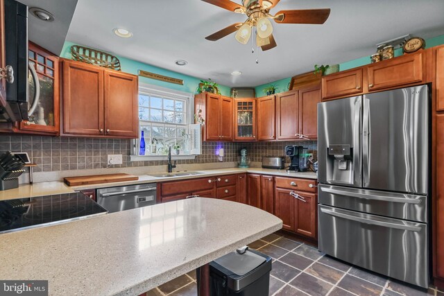 kitchen with a sink, light countertops, glass insert cabinets, appliances with stainless steel finishes, and backsplash