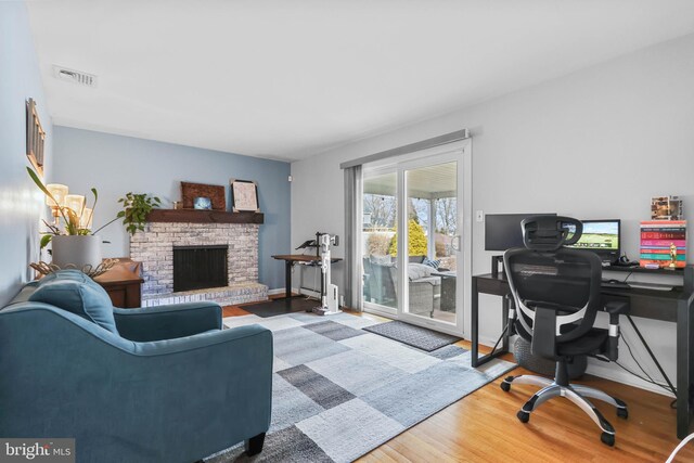 office space featuring visible vents, a brick fireplace, baseboards, and wood finished floors