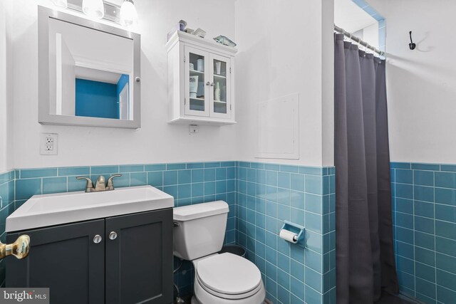 full bathroom featuring tile walls, toilet, a shower with shower curtain, wainscoting, and vanity