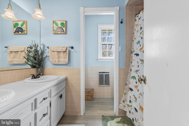 bathroom featuring wood finished floors, double vanity, a sink, wainscoting, and tile walls