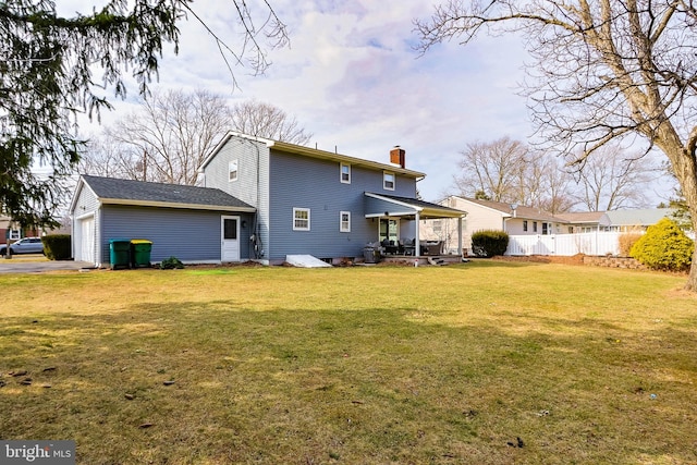 back of house with an attached garage, fence, a yard, and a chimney