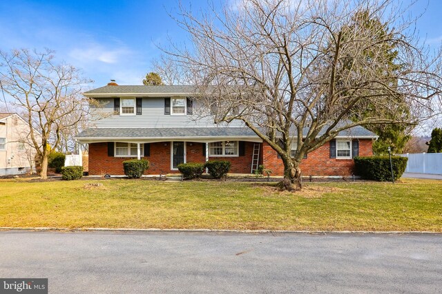 traditional home with brick siding, a chimney, a front yard, and fence