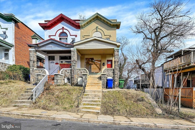 view of front of property featuring stone siding, stairs, covered porch, and stucco siding