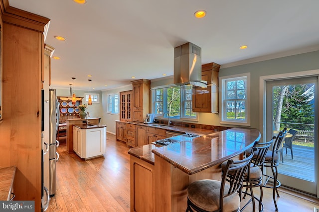 kitchen with a peninsula, island exhaust hood, ornamental molding, a sink, and brown cabinets