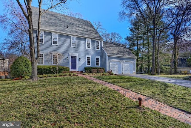 colonial home featuring aphalt driveway, an attached garage, and a front lawn