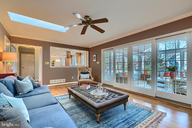 living room featuring visible vents, wood finished floors, a skylight, and ornamental molding