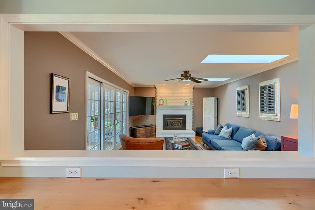 living area with a skylight, ornamental molding, a fireplace, and ceiling fan