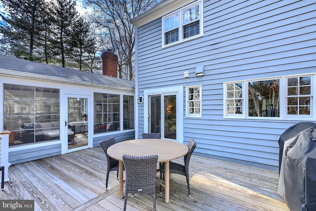 wooden deck with outdoor dining area, a sunroom, and a grill