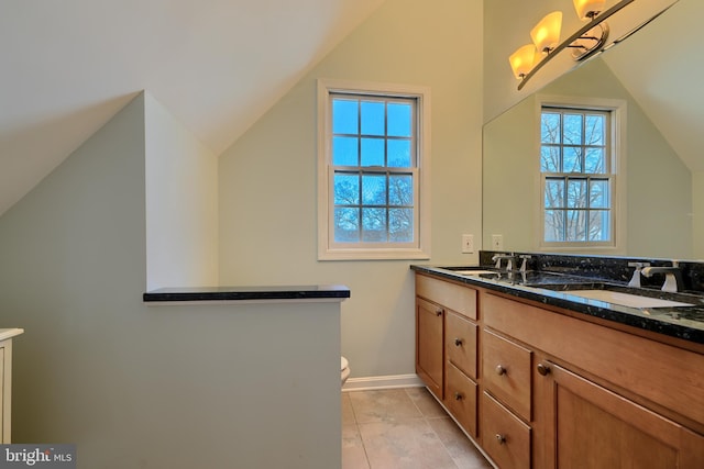 bathroom with baseboards, toilet, lofted ceiling, double vanity, and a sink