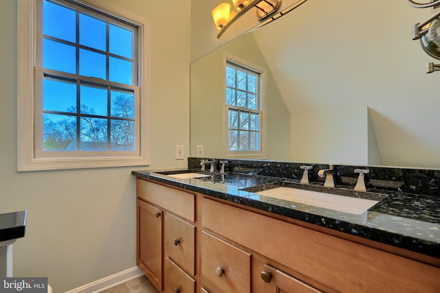 bathroom with lofted ceiling, double vanity, baseboards, and a sink