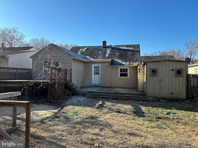 back of property featuring a deck, an outdoor structure, fence, a storage unit, and a chimney