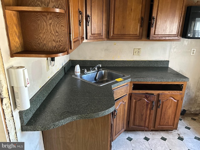 kitchen featuring brown cabinetry, dark countertops, a sink, and open shelves