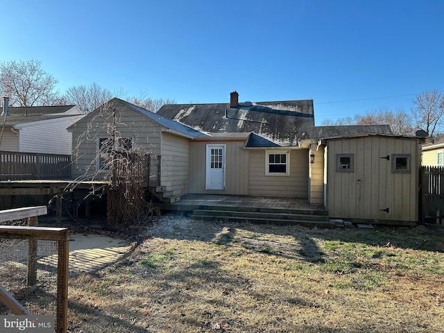 rear view of house with a deck, an outbuilding, fence, a storage unit, and a chimney