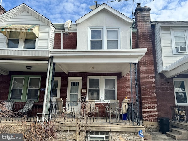 view of property with a porch, a chimney, brick siding, and stucco siding