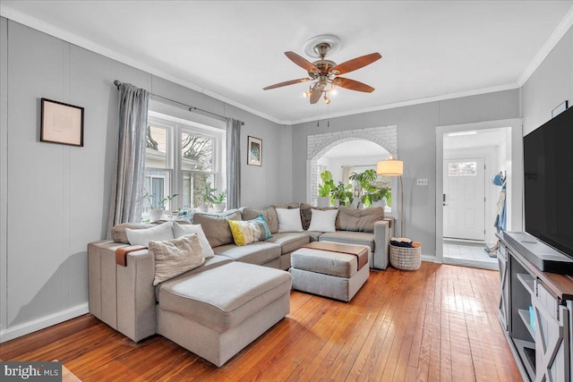 living area with arched walkways, light wood-style flooring, a ceiling fan, baseboards, and ornamental molding