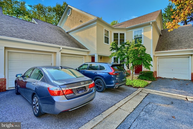 traditional home with a garage, roof with shingles, driveway, and stucco siding