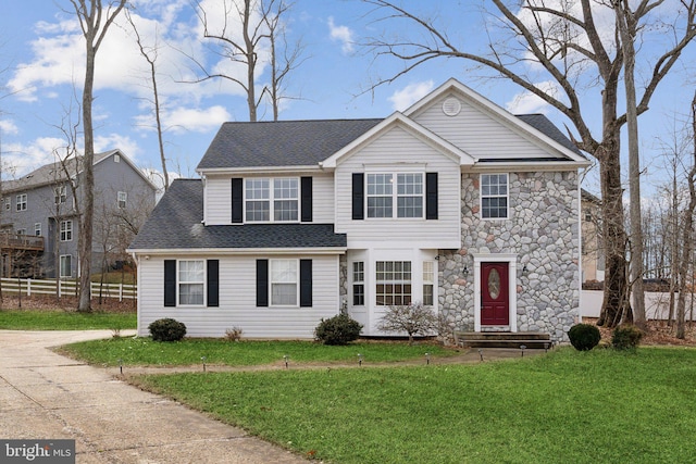 view of front of home featuring stone siding, roof with shingles, fence, and a front lawn