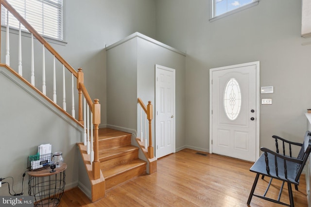 foyer with stairs, a towering ceiling, and light wood-style flooring