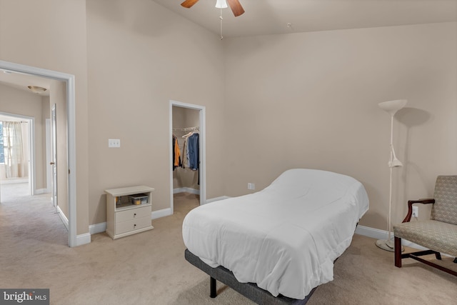 bedroom featuring baseboards, a closet, a walk in closet, and light colored carpet