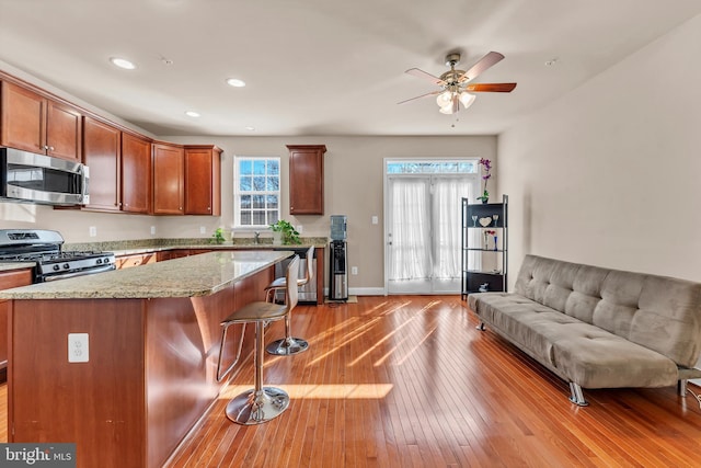 kitchen with light stone counters, stainless steel appliances, a center island, hardwood / wood-style floors, and a kitchen bar