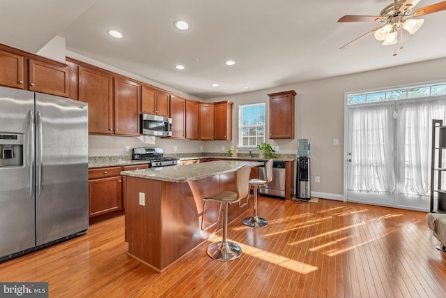 kitchen with appliances with stainless steel finishes, a kitchen breakfast bar, a kitchen island, and light wood finished floors