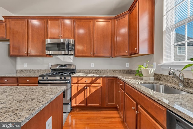 kitchen featuring stainless steel appliances, light stone counters, a sink, and light wood-style flooring