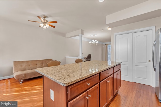 kitchen featuring light stone counters, ceiling fan with notable chandelier, light wood-style floors, freestanding refrigerator, and a center island