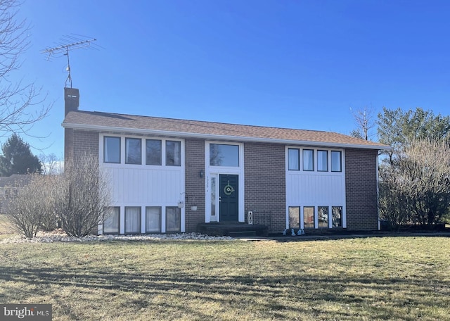 raised ranch with a front lawn, brick siding, and a chimney