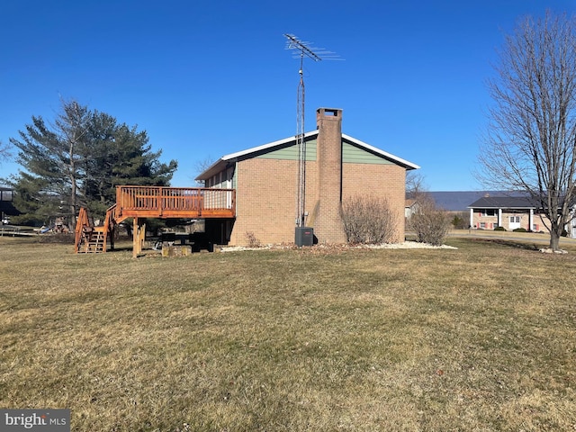 rear view of house with brick siding, a lawn, a chimney, and a deck