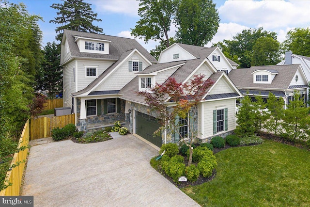 shingle-style home featuring driveway, stone siding, fence, a front yard, and a shingled roof